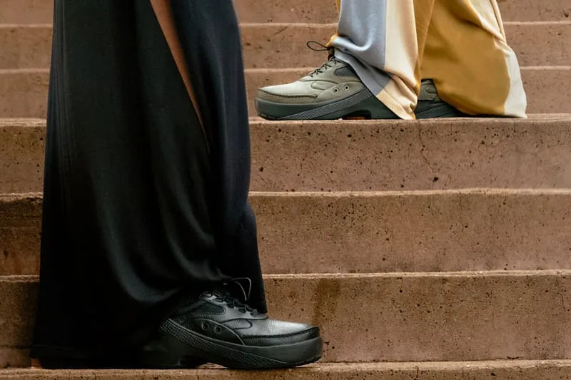 On-foot view of black shoe on stone steps, with a grey-green pair on another person above, x Kiko Kostadinov