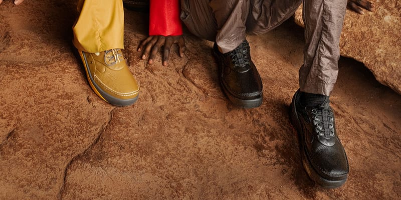 On-foot view of two people crouching on red rock, one in mustard shoes, one in black leather shoes, x Kiko Kostadinov