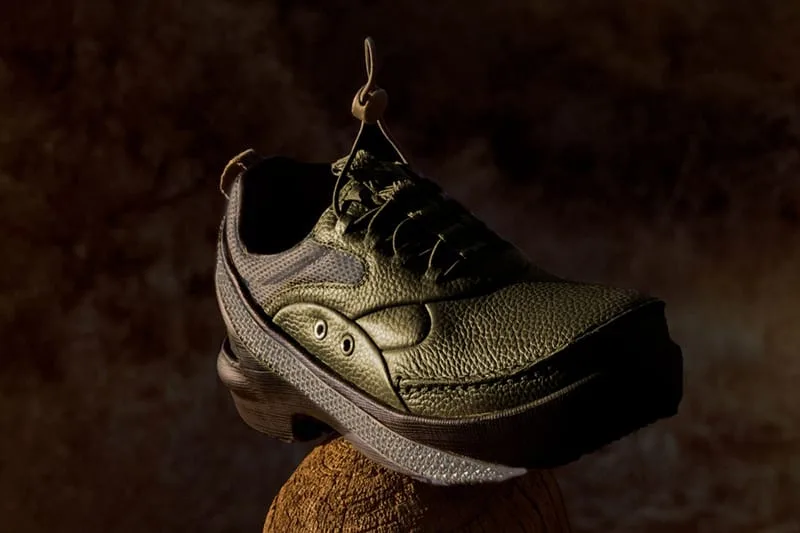 Angled view of olive pebbled-leather shoe with bungee laces and ridged grey midsole, perched on a wooden stump, x Kiko