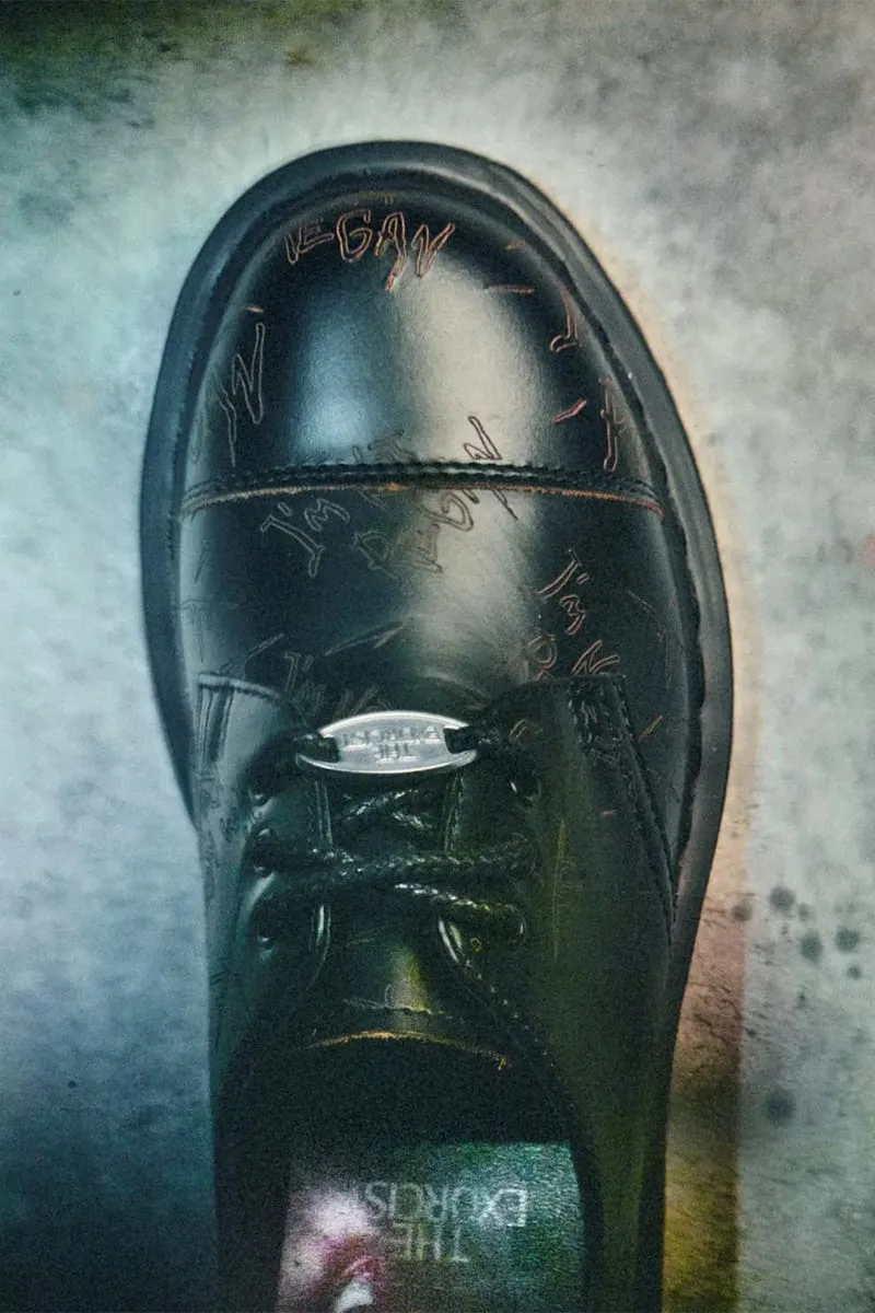 Top-down view of black leather toe cap with etched red scribbles and a silver lace tag, The Exorcist