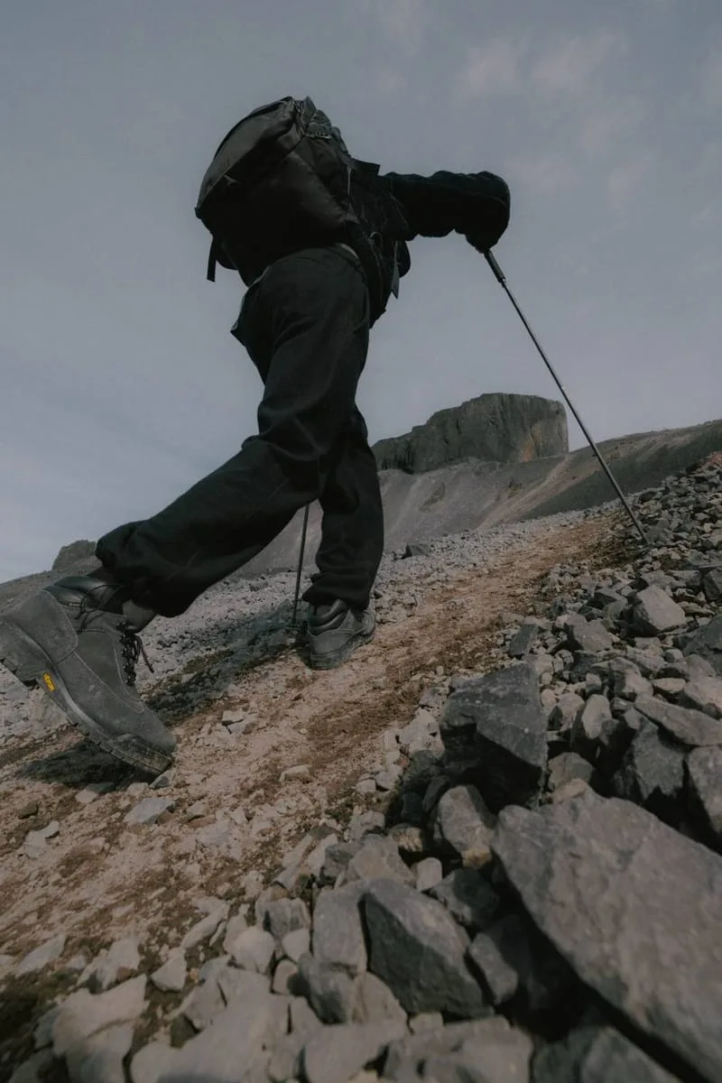 Low-angle on-foot hiking shot on a rocky slope, backpack and trekking pole, Black