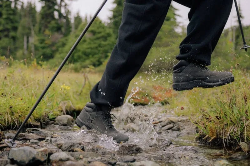 On-foot shot stepping through a stream, trekking pole, grassy meadow, water splash, Black
