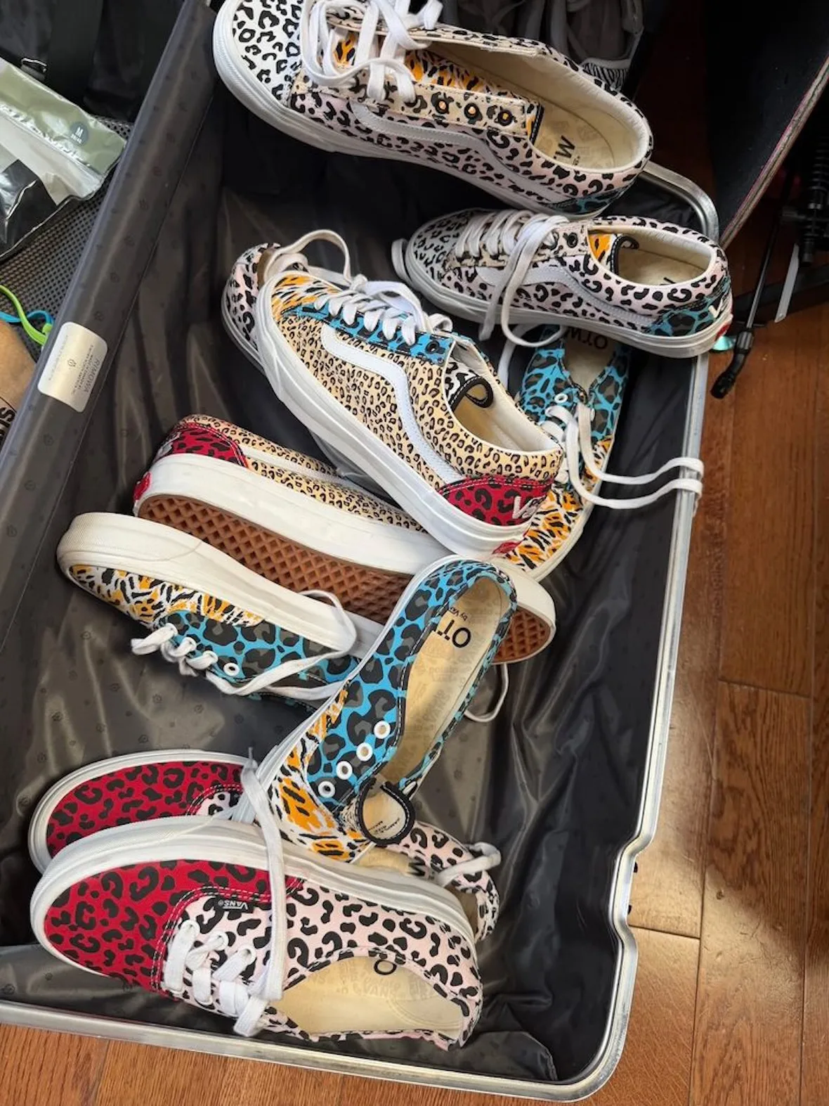 Top-down view of leopard-print sneakers in red, cream, teal and orange piled in an open suitcase, Cheetah Print