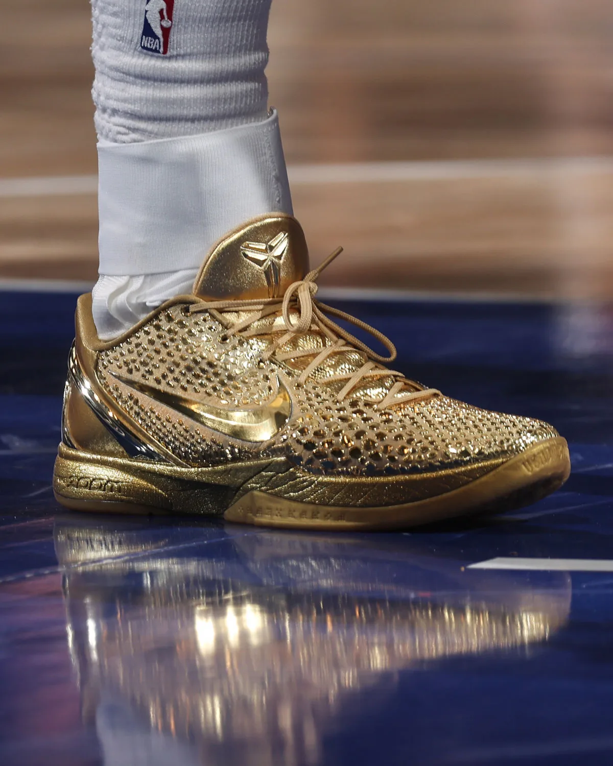 Lateral on-foot view of gold shoe on a blue court with reflection, mirrored swoosh and tan laces, Ring Night