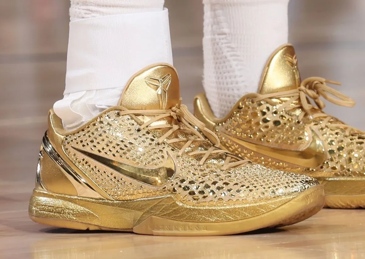 Lateral on-foot view of both gold shoes on a wood court, gold heel tab with logo and tan laces, Ring Night