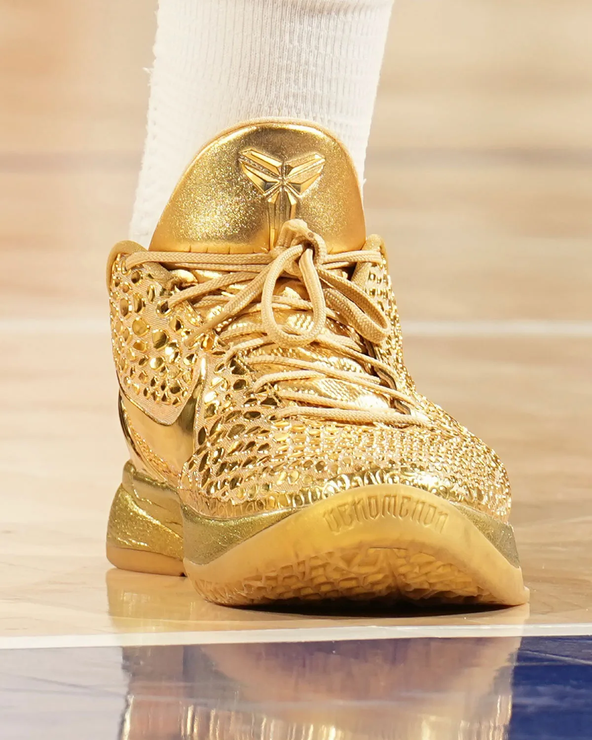 Toe-on view on court of gold shoe, heel tab logo, tan laces and gold outsole with lettering near the toe, Ring Night