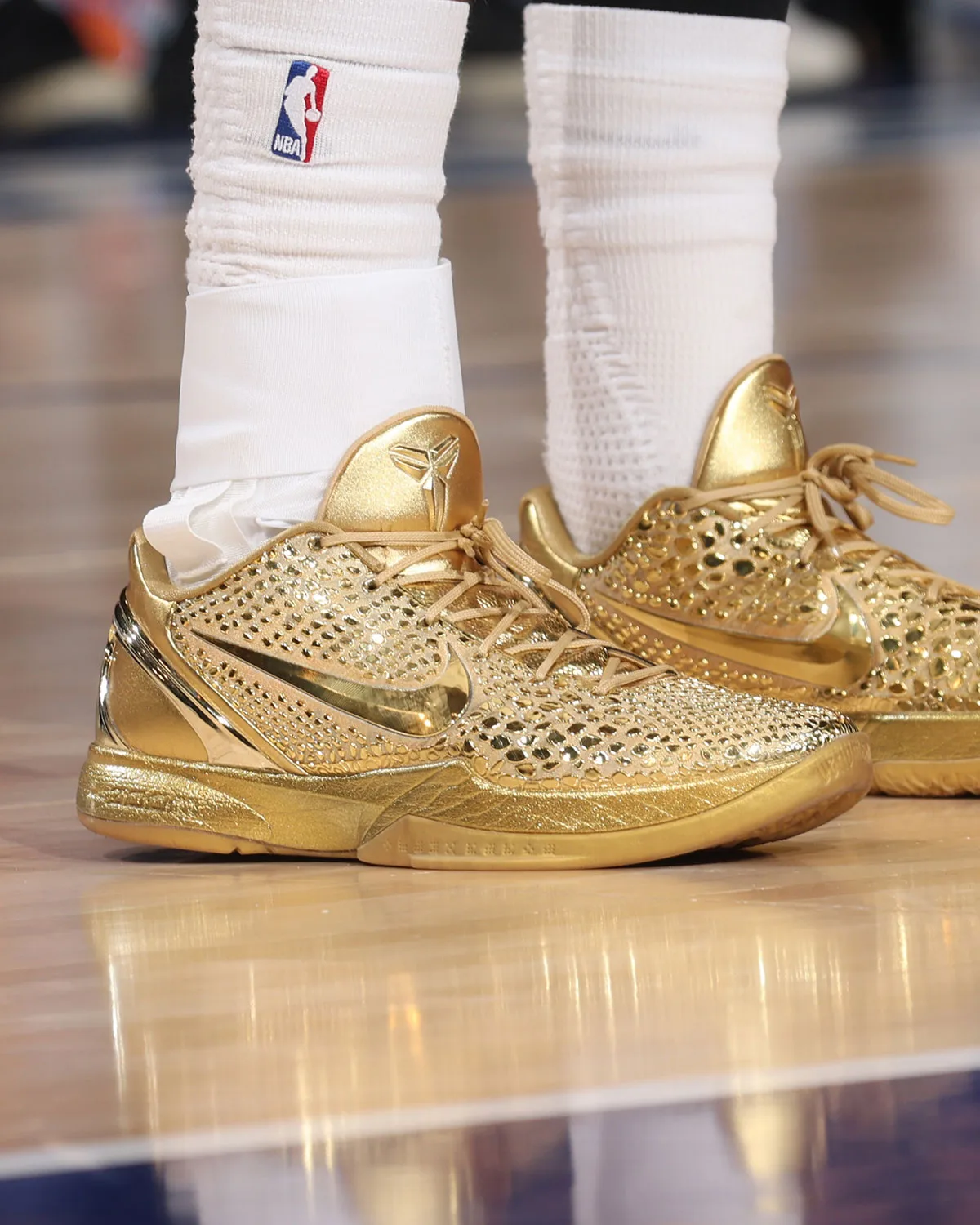 Pair on-foot on a wood court, gold perforated uppers, mirrored swoosh and white socks with NBA logo, Ring Night