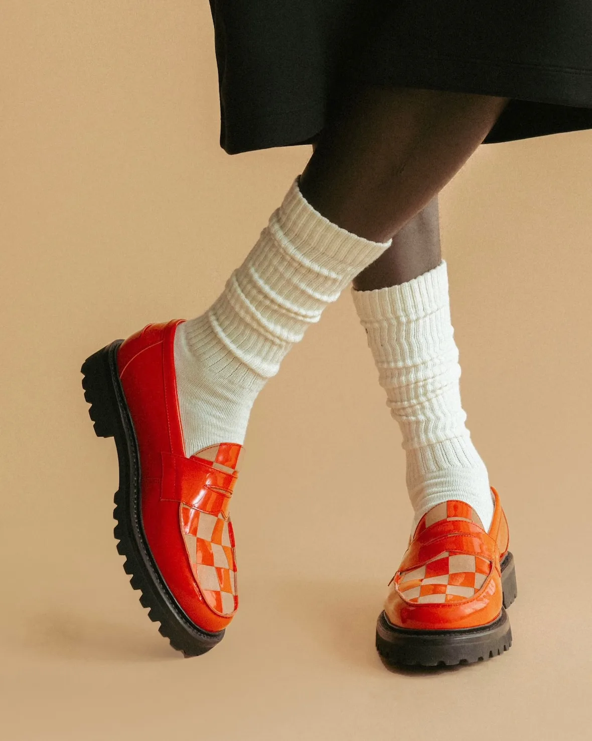 On-foot pair of glossy orange-red checkered loafers with chunky black soles and white slouch socks, Candy Apple