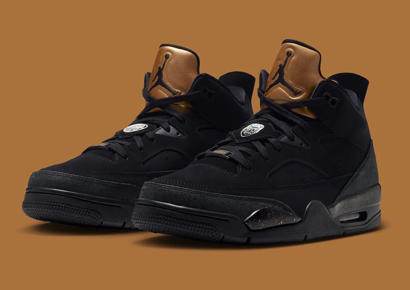 Pair, three-quarter view of black nubuck sneakers with gold tongues on a tan backdrop, Jordan Son of Mars Low “Gold Tongue”