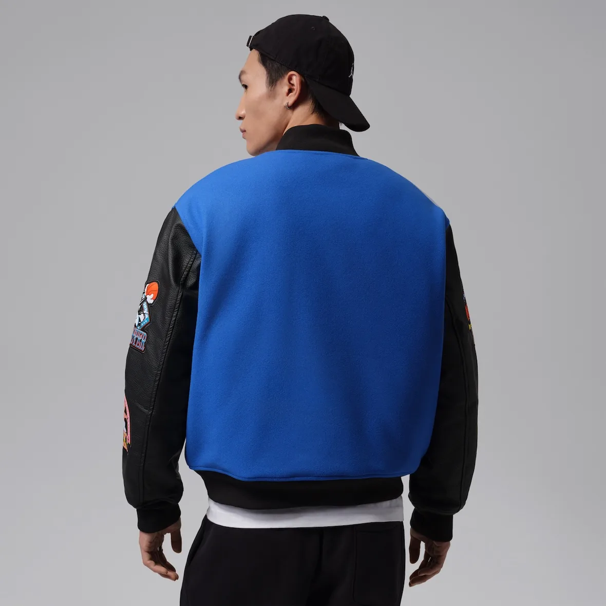On-model back view of plain blue jacket body with patches on black leather sleeves, Varsity Royal/Black