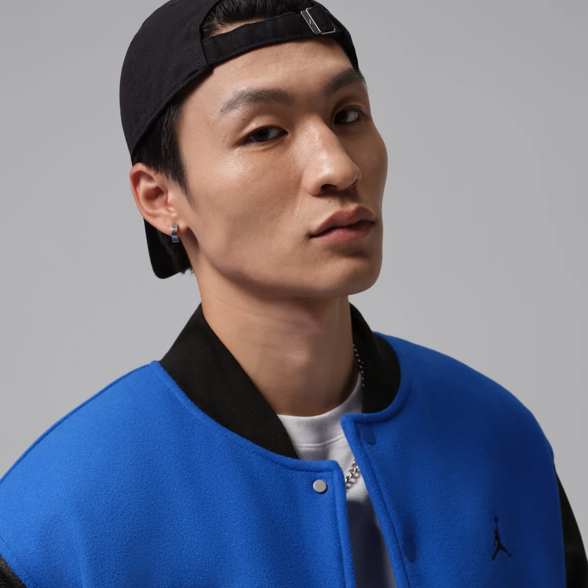 On-model close-up of collar and Jumpman logo on blue jacket, black cap and earring, Varsity Royal/Black