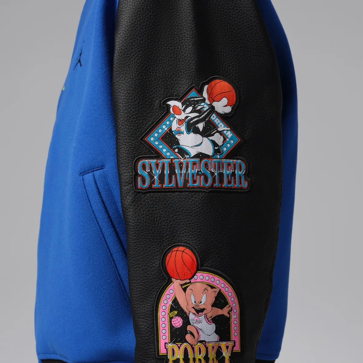 Detail of black leather sleeve with Sylvester and Porky patches beside blue body, Varsity Royal/Black