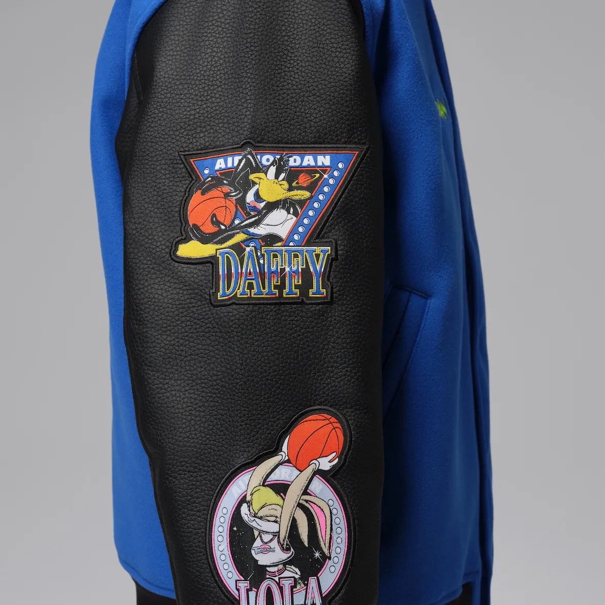 Detail of black leather sleeve with Daffy and Lola patches against blue body, Varsity Royal/Black