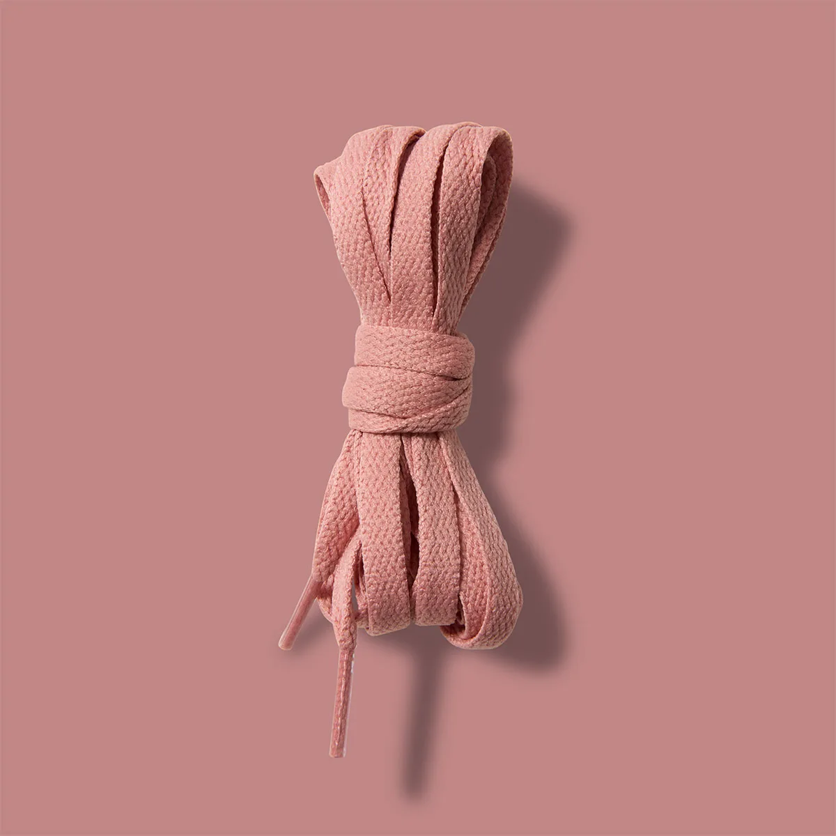 Detail of bundled pink spare laces against a dusty pink background, Rust Pink