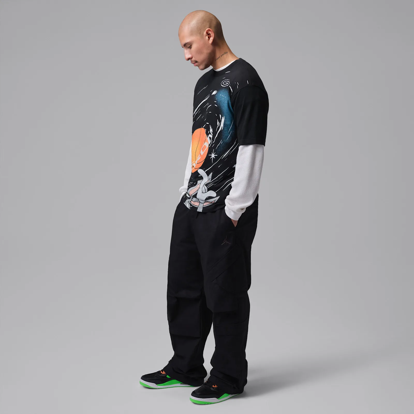 On-foot full-body shot, person in black graphic tee and trousers wearing black and neon green sneakers, Space Jam