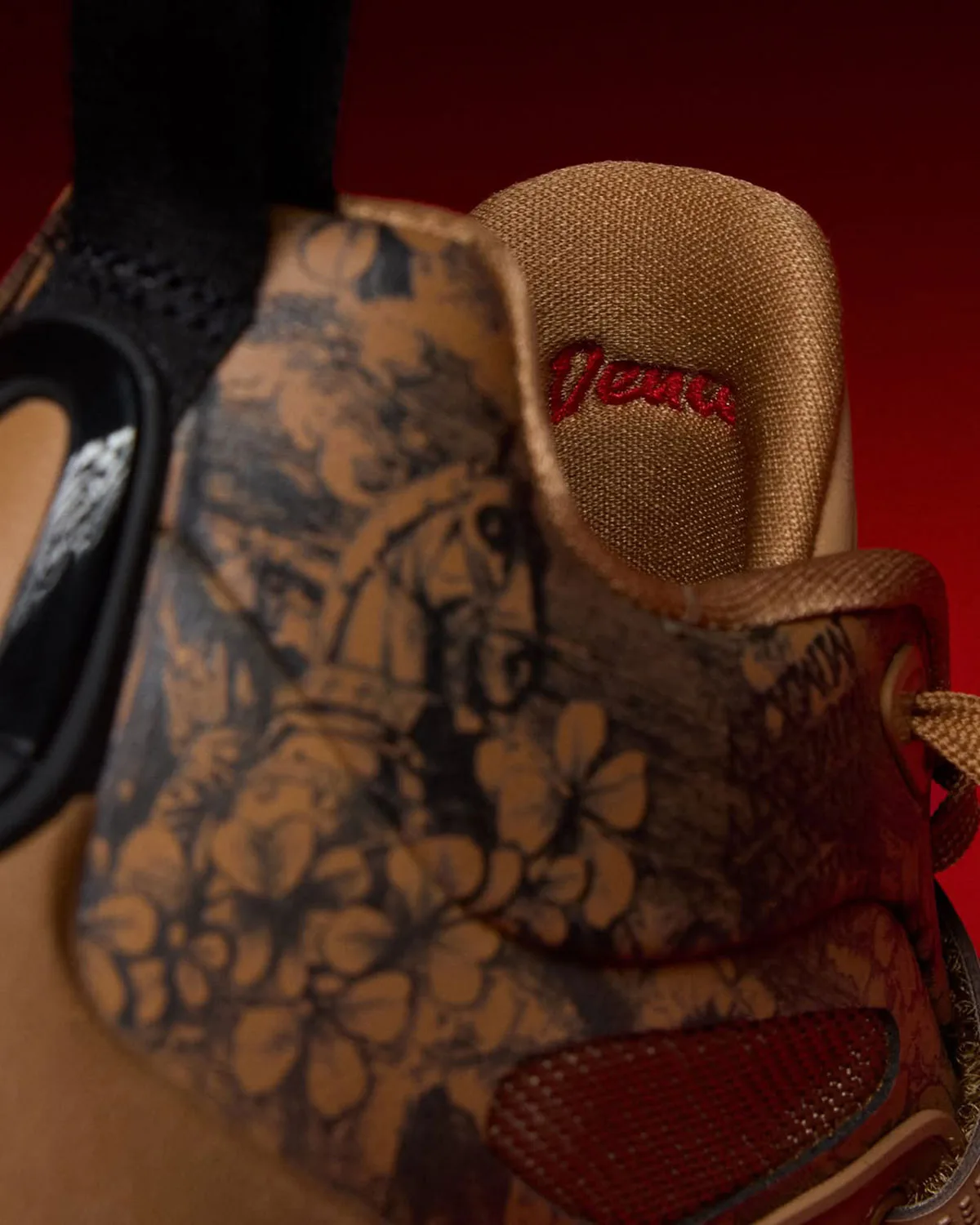 Close detail of tan floral etched leather, red script on tongue lining, red mesh panel, black heel tab, Laser