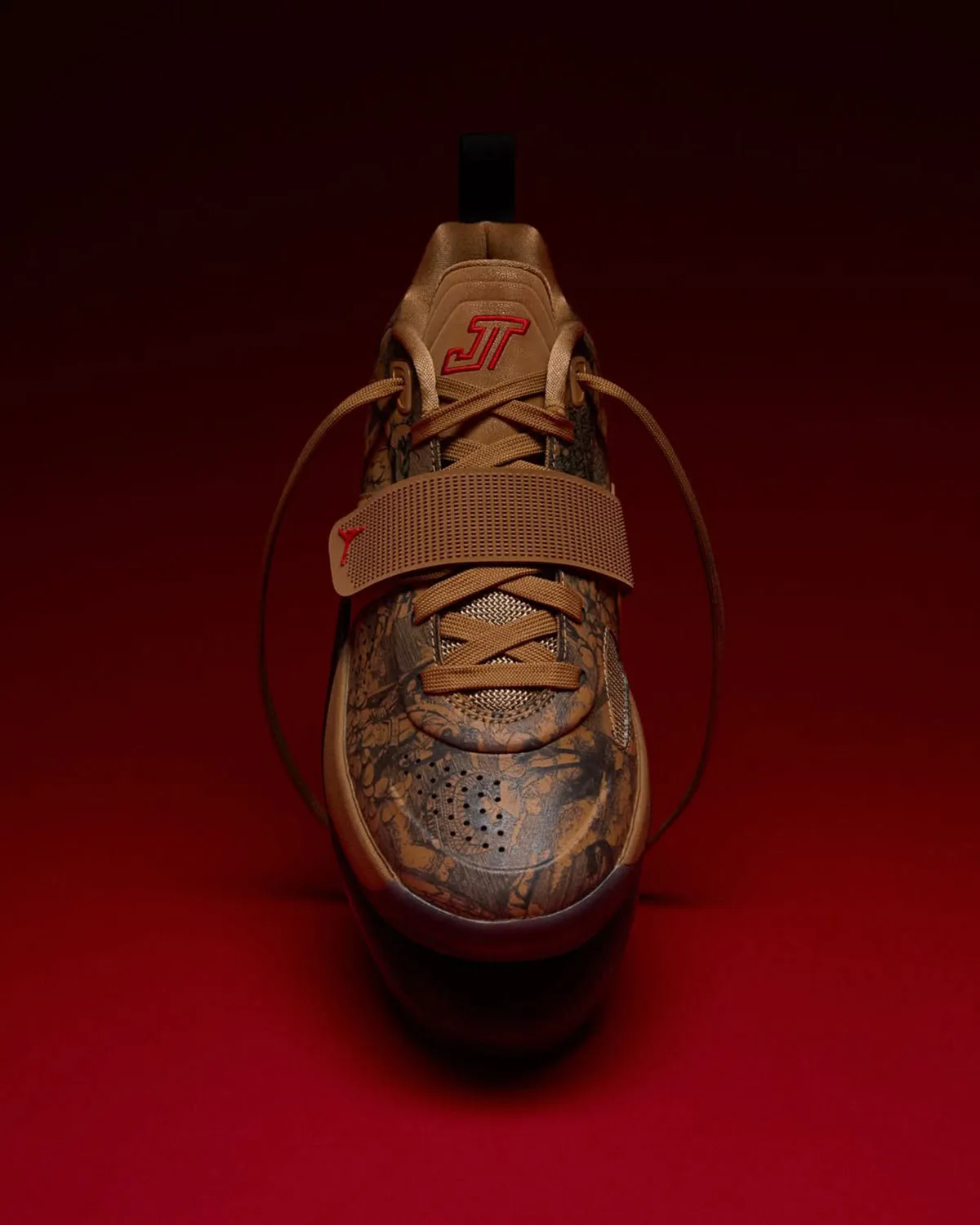 Toe-on front view, tan floral upper, wide hook-and-loop strap, red JT tongue logo, looped laces, Laser