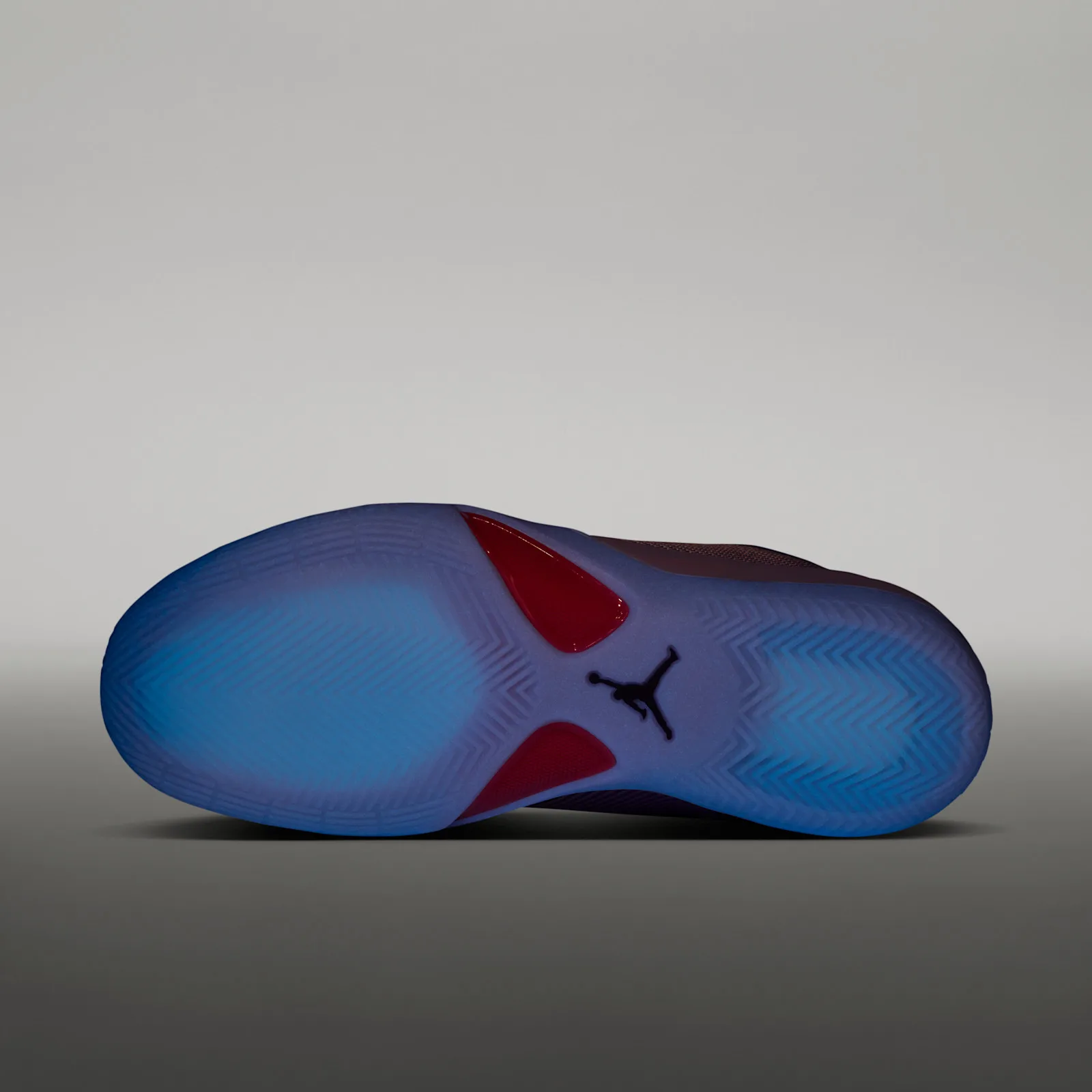 Outsole under a dark glow effect, blue-lit translucent tread with red shank pieces and black Jumpman logo, Bright Concord