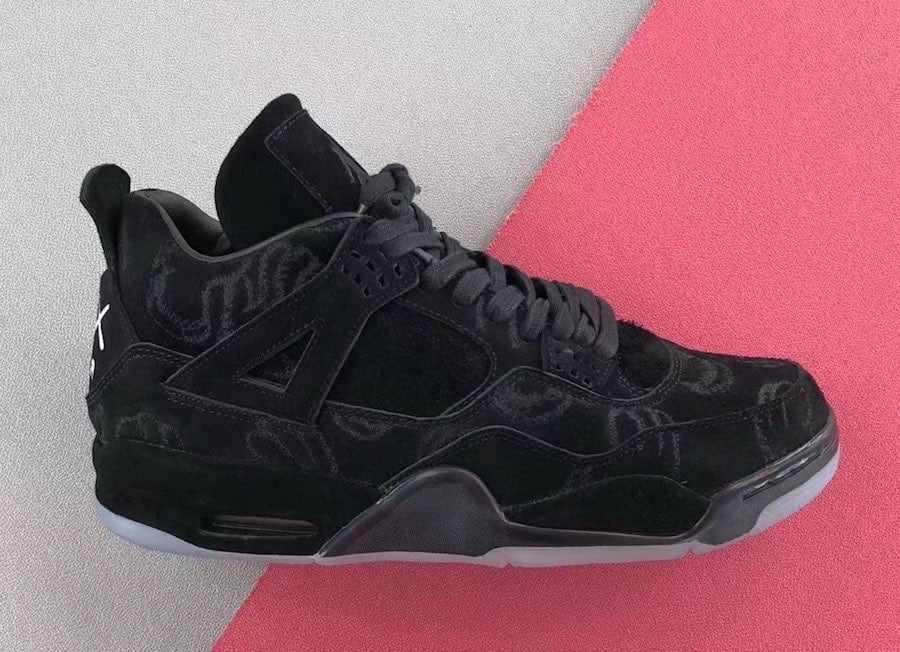 Lateral view of black suede sneaker with faint embroidered pattern, icy translucent sole, grey and pink backdrop, Dark Grey