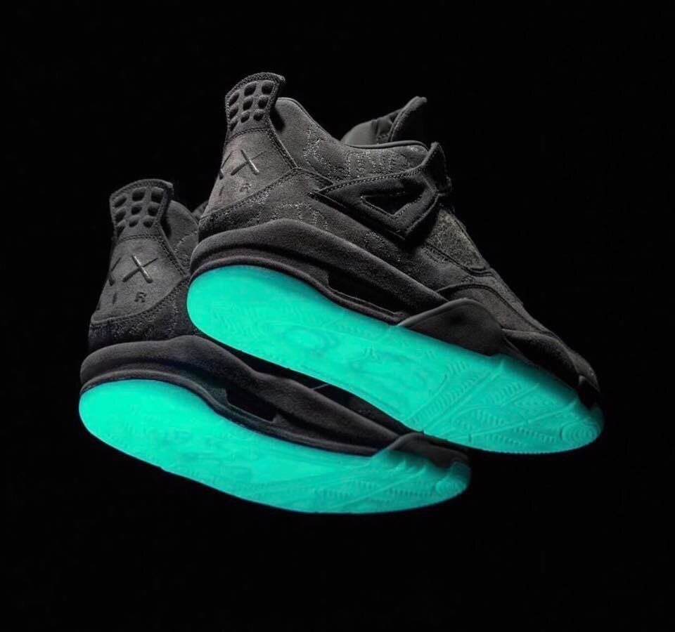 Outsole view of two grey suede sneakers with glowing teal-green soles on black background, Dark Grey
