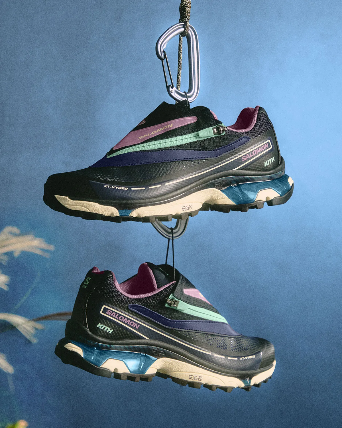 Pair of navy shoes with mint zips and blue heel windows hanging from carabiners, blue backdrop, Winter 2026 Collection