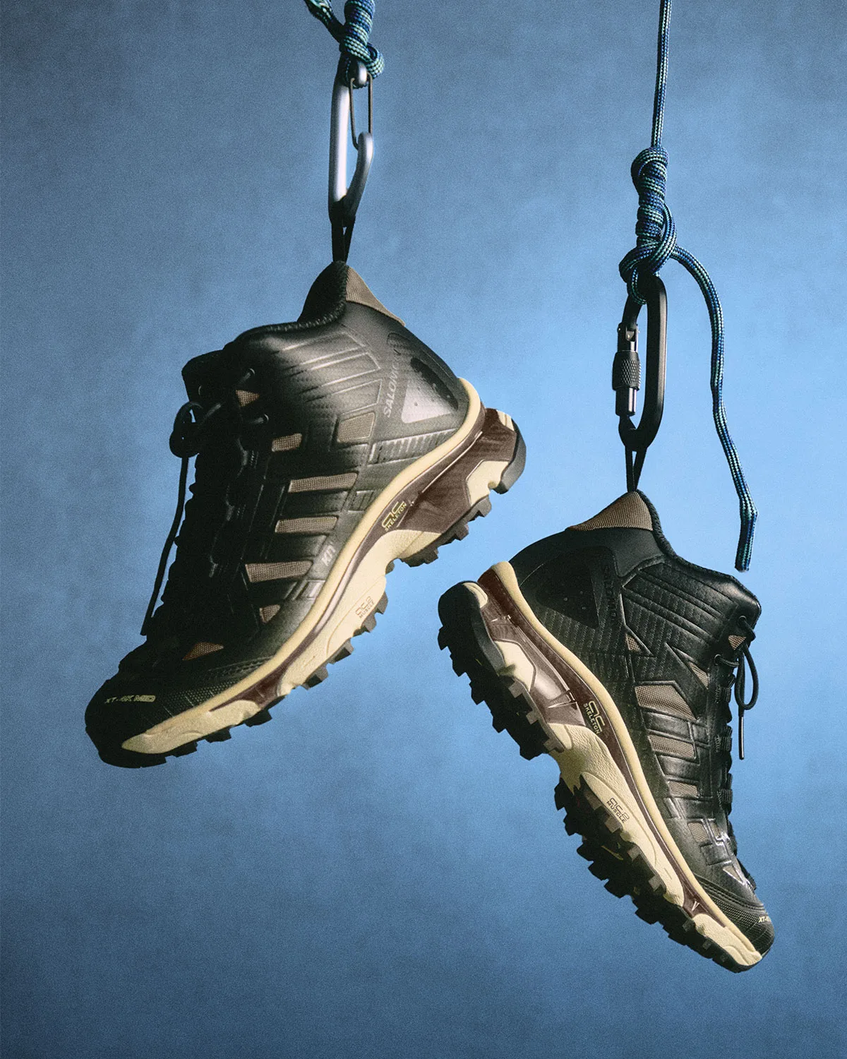 Pair of black mid-height boots with tan stripes hanging from carabiners and blue rope, Winter 2026 Collection