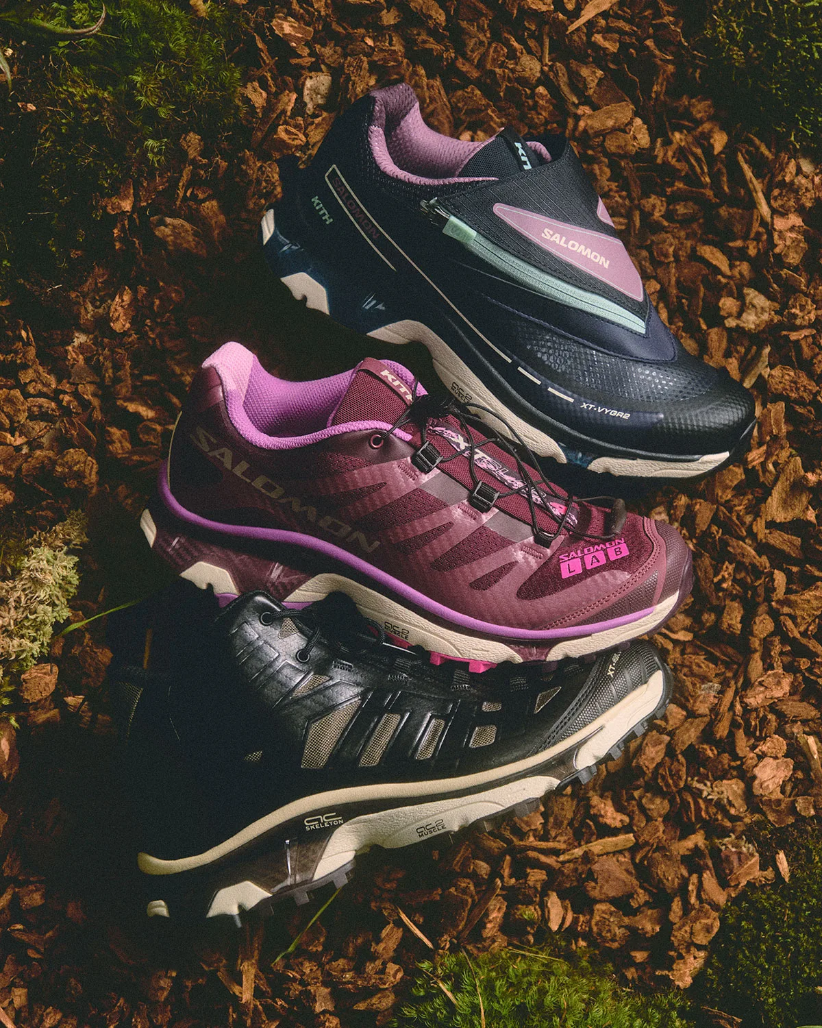 Three shoes stacked on bark mulch and moss: navy zip shoe, burgundy shoe, black shoe, Winter 2026 Collection