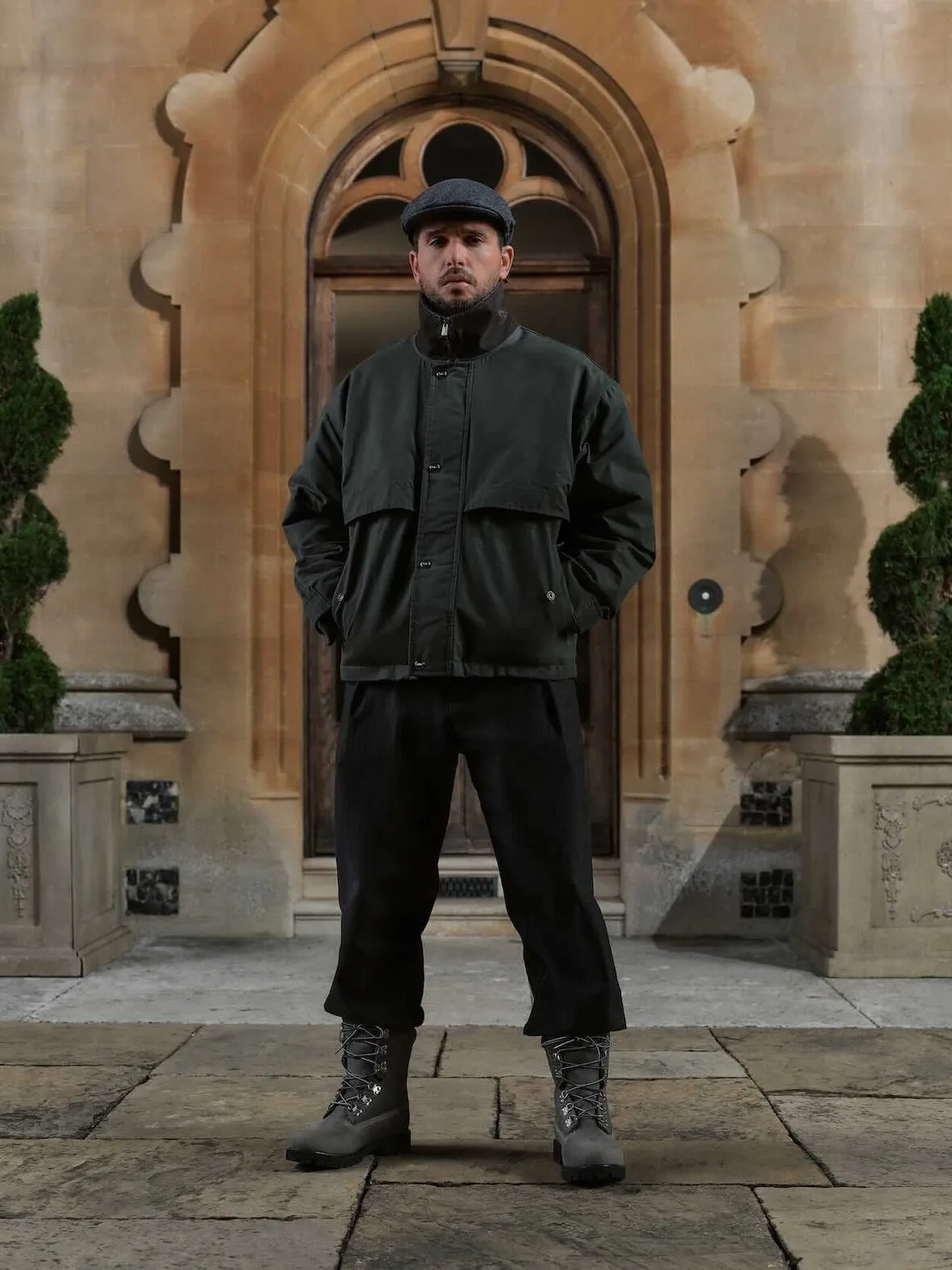 On-model full-length, dark green jacket, black trousers, grey lace-up boots with black lug soles on stone paving, Winter