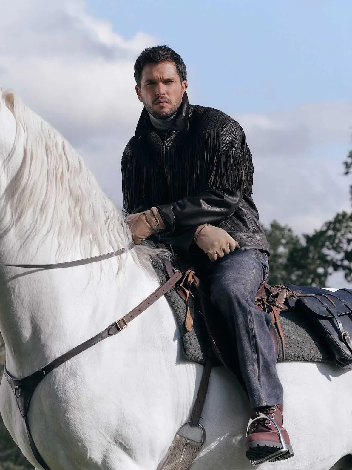 On-model, seated on white horse, black woven fringed jacket, tan gloves, dark red lace-up boot in a stirrup, Winter 2026