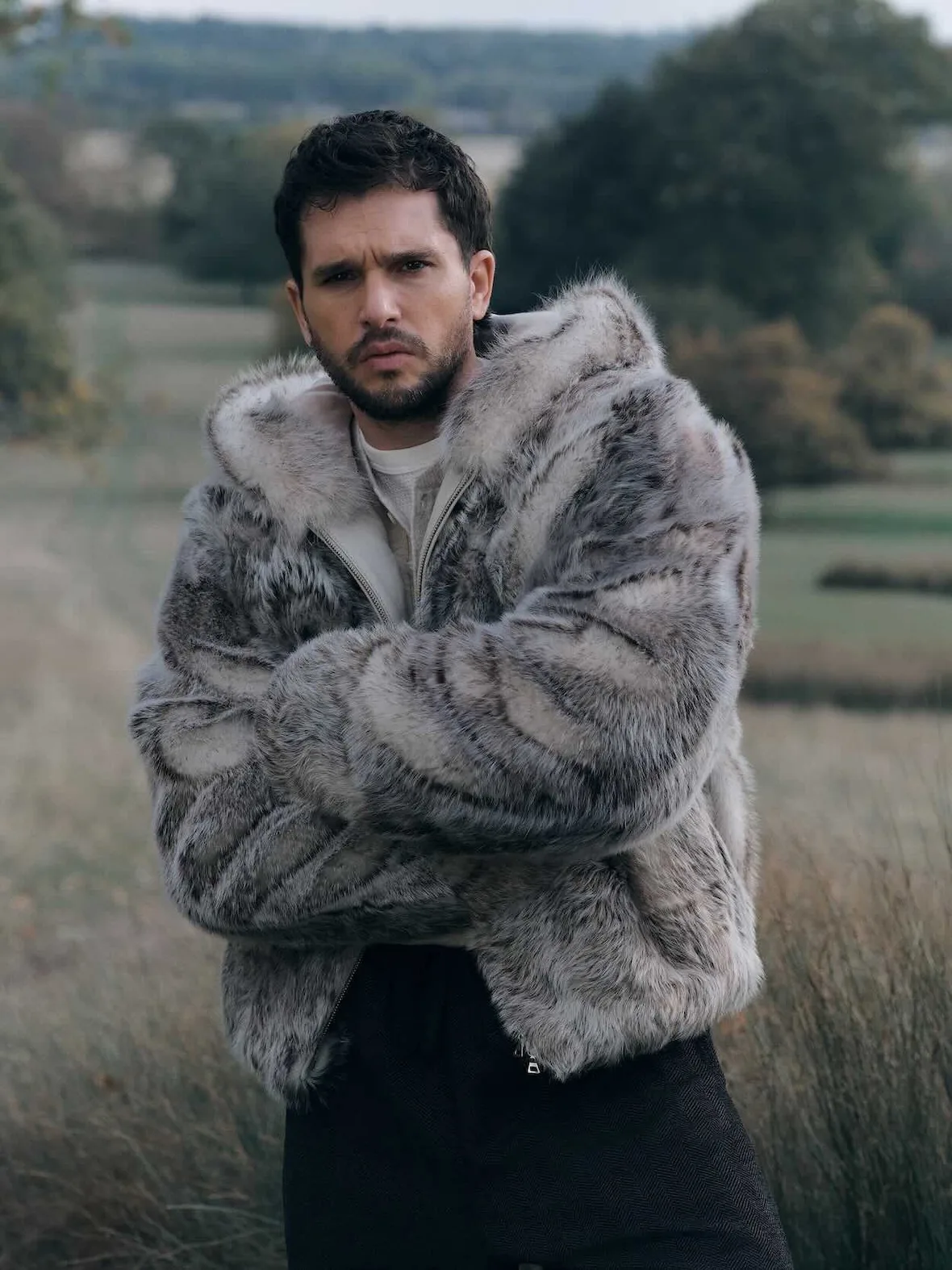 On-model close portrait, grey and white faux fur hooded jacket, arms crossed, blurred meadow behind, Winter 2026 Collection