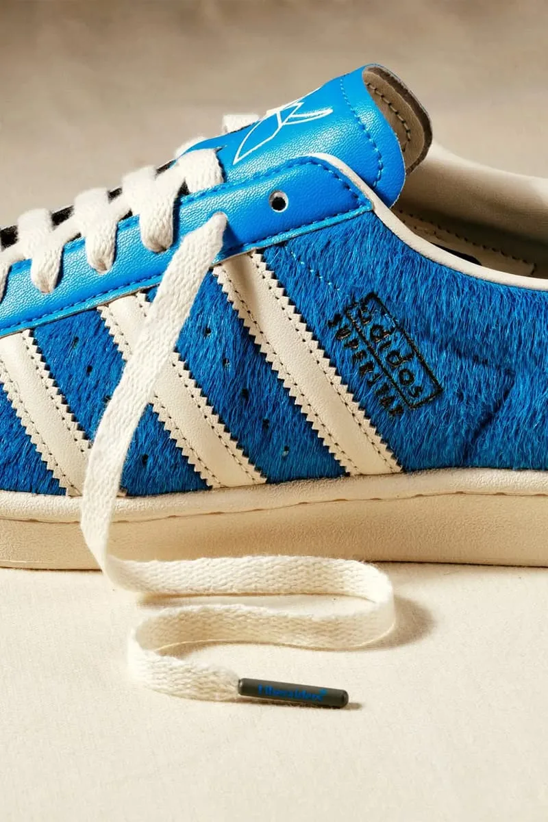 Lateral detail: blue hairy upper, cream three stripes, black Superstar logo, loose lace on floor, Blue
