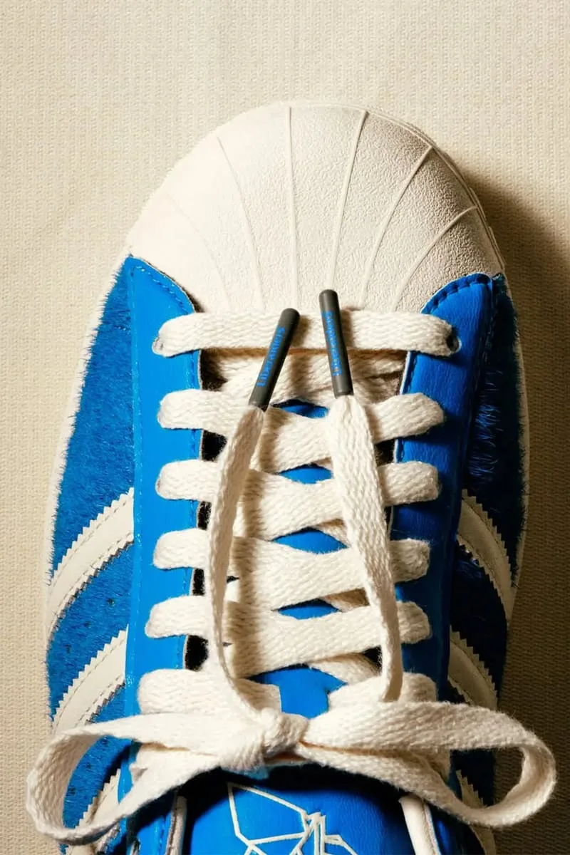 Top-down toe detail: cream laces, grey lace tips, shell toe and crane logo on tongue, Blue