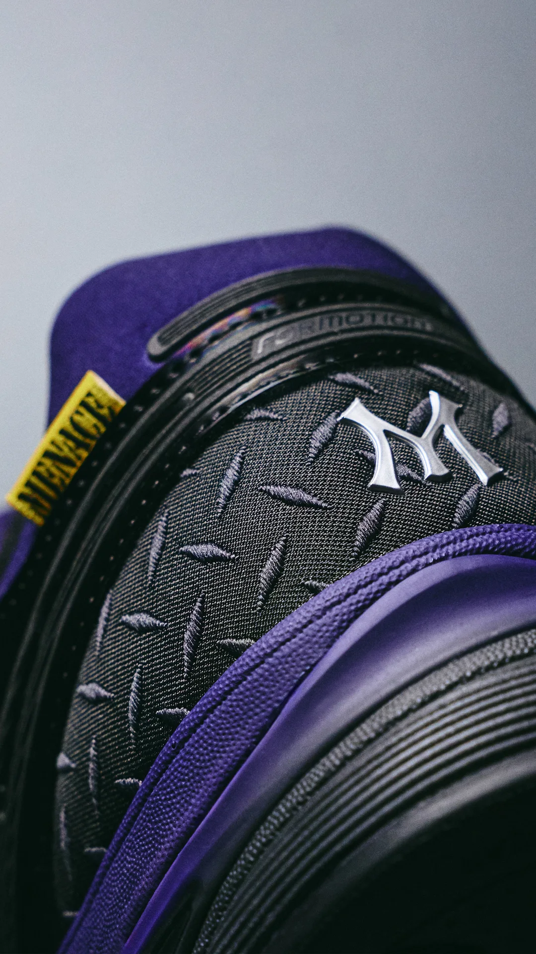 Close-up of the diamond-plate heel counter with a silver M emblem, a yellow MENACE tab and purple heel padding