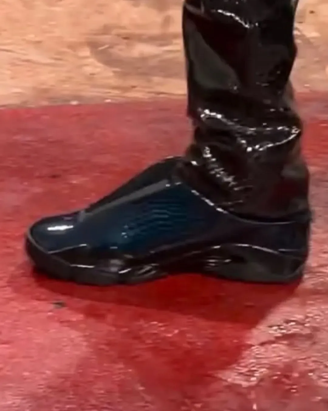 Lateral on-foot view of dark navy-teal patent croc mule with black sole on a red floor, Patent Croc