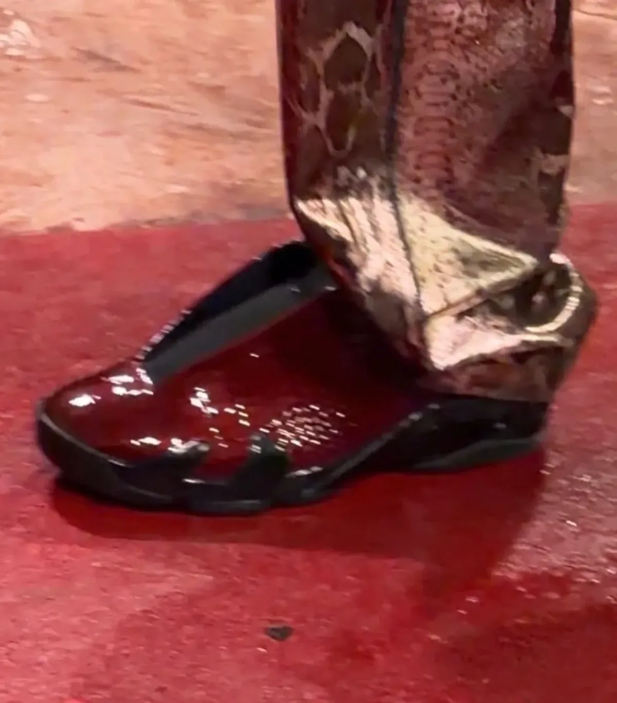 Top-down on-foot view of glossy burgundy mule with black trim, snakeskin trousers, red floor, Patent Croc