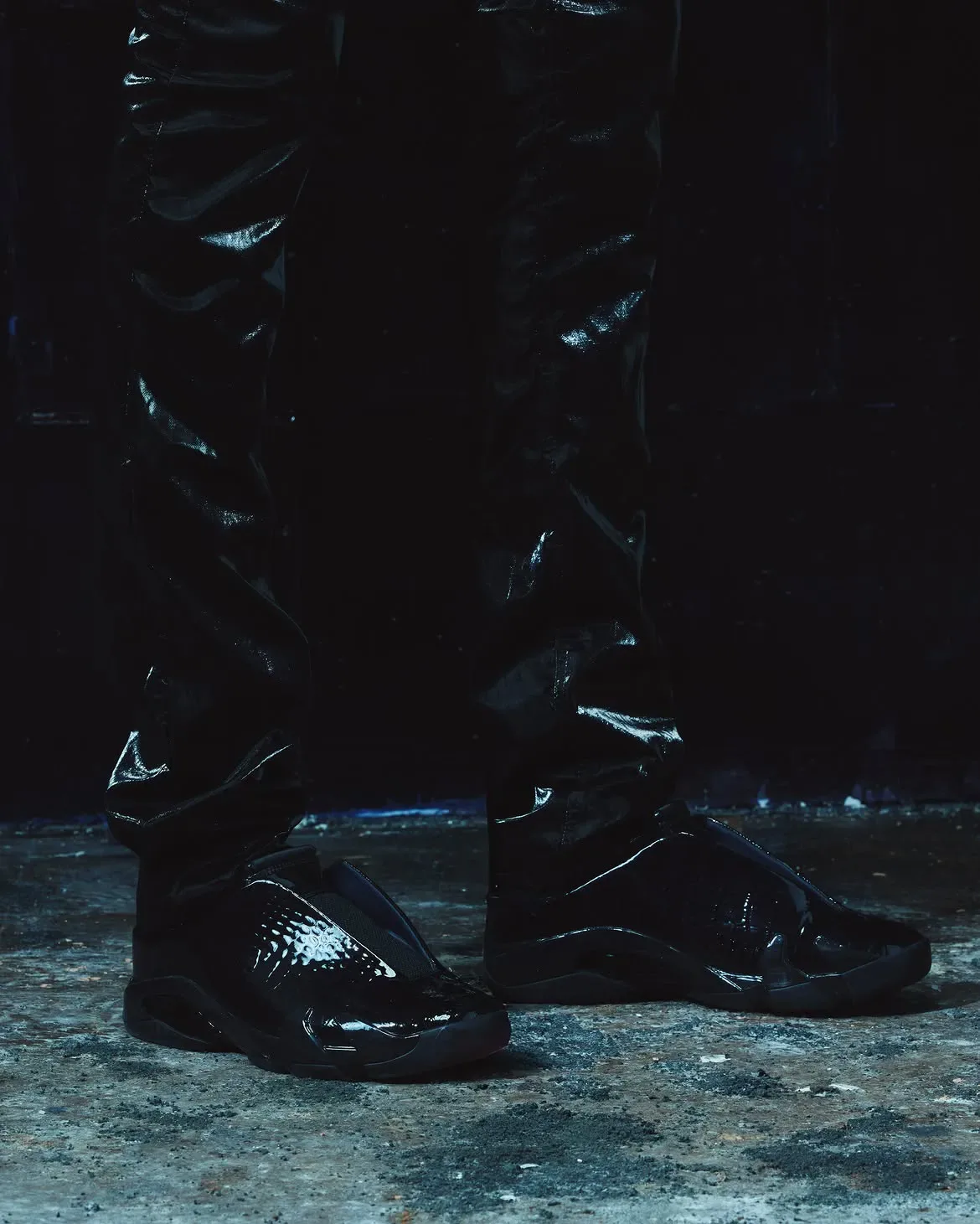 On-foot pair in dark studio, all-black patent croc-texture mules with glossy black trousers, Patent Croc