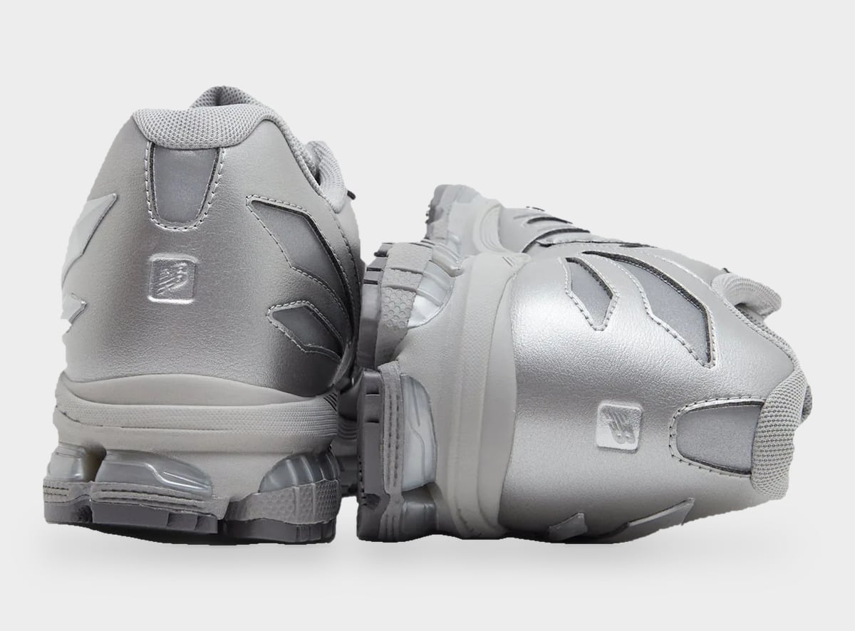Heel view of a silver pair with metallic NB logo patches and clear heel cushioning pods, Liquid Metal