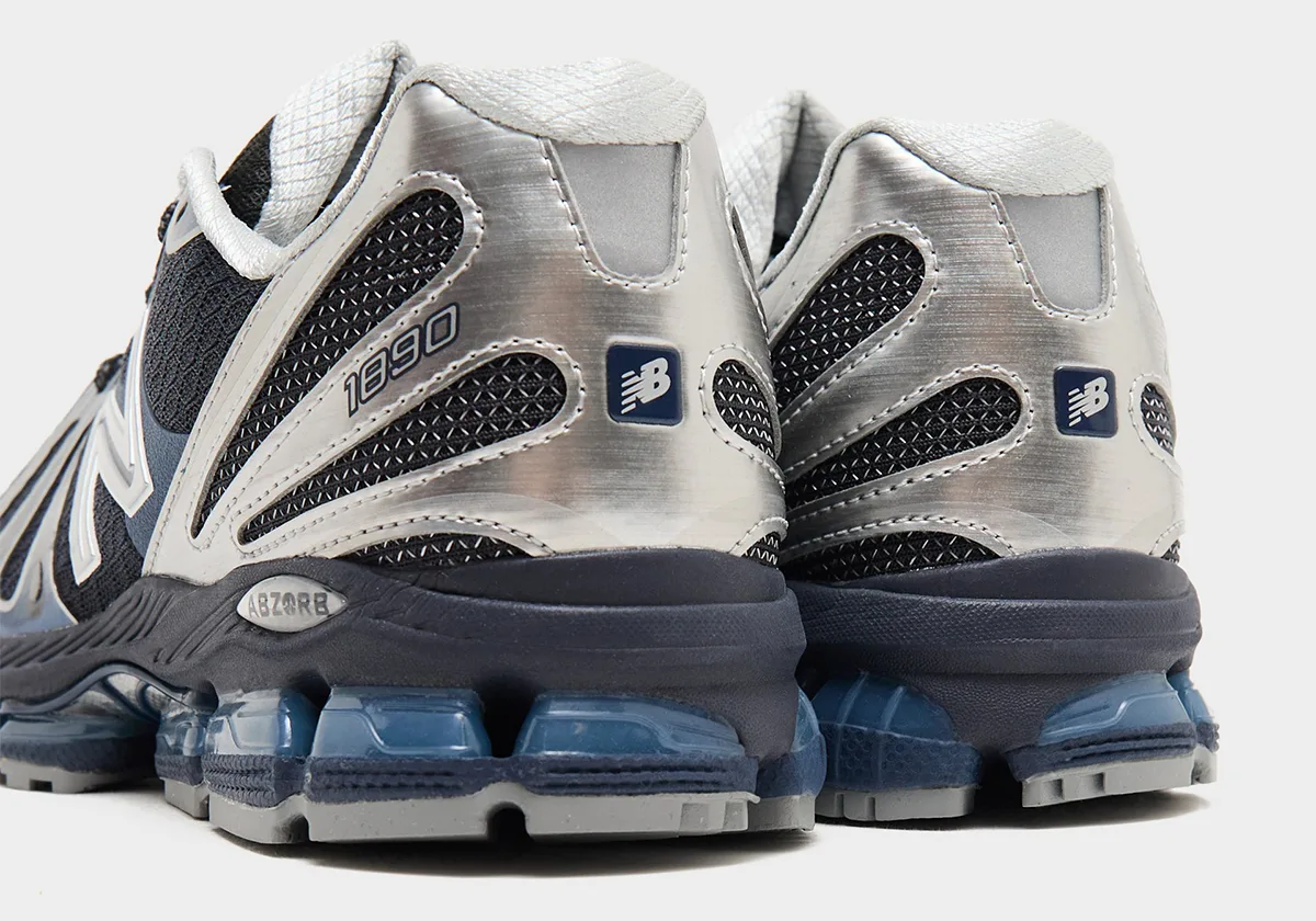 Heel view of both shoes, brushed silver heel counters, navy New Balance tags, 1890 text, blue cushioning pods, Metallic Blue