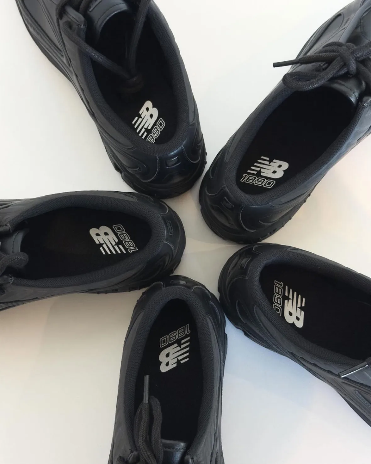 Five black shoes arranged in a circle on white, showing NB 1890 logos printed on insoles, Black Leather