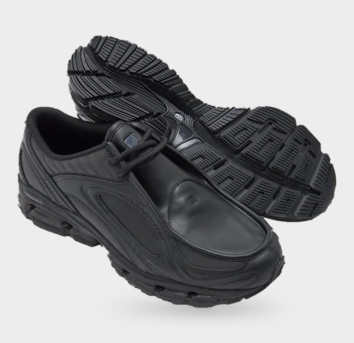 Pair with one shoe on its side showing black patterned outsole and N logo on toe, Black Leather