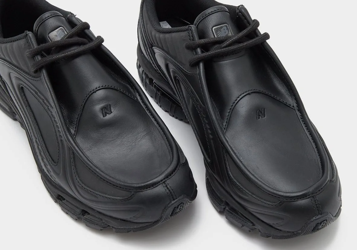 Close-up of two black leather toe boxes with debossed N logos and black laces on white, Black Leather