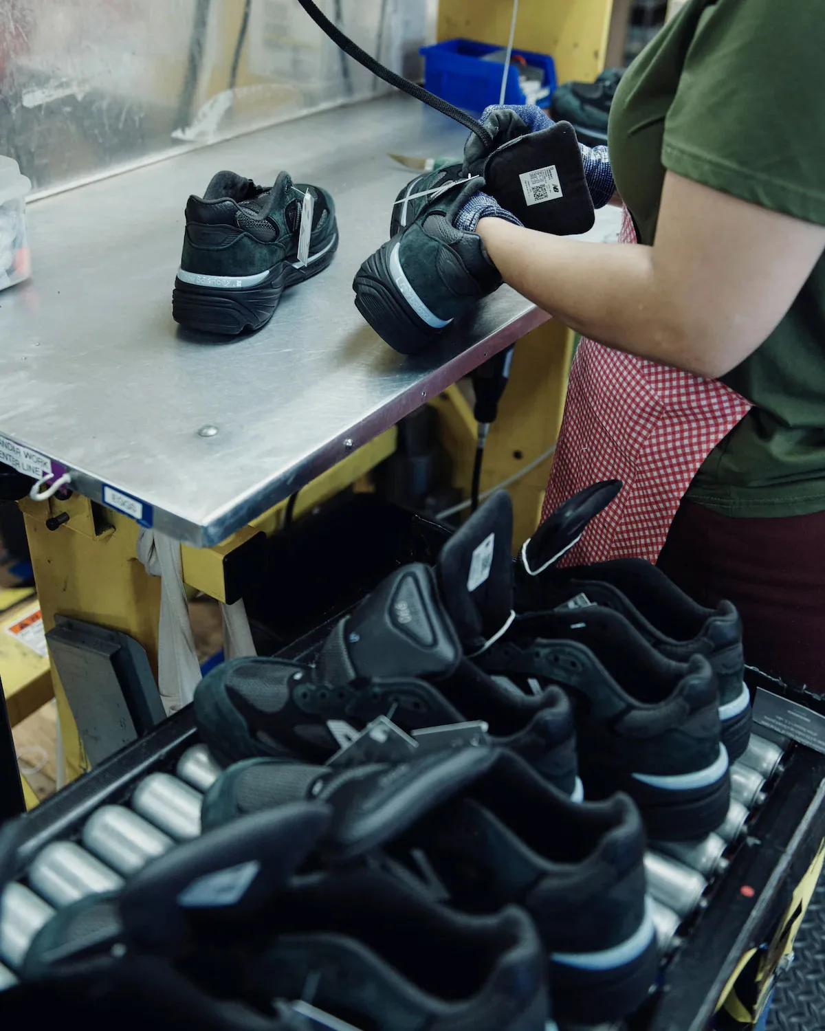 Factory worker in gloves handling black sneakers, more pairs on a roller rack, Black/Silver
