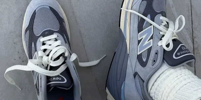 Top-down pair on concrete, grey-blue suede and mesh, cream laces, N logo and white sock, New Balance 990v7