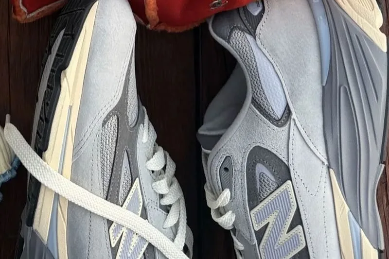 Close-up of pair on dark wood, light grey suede, lavender N logo and cream midsole, New Balance 990v7