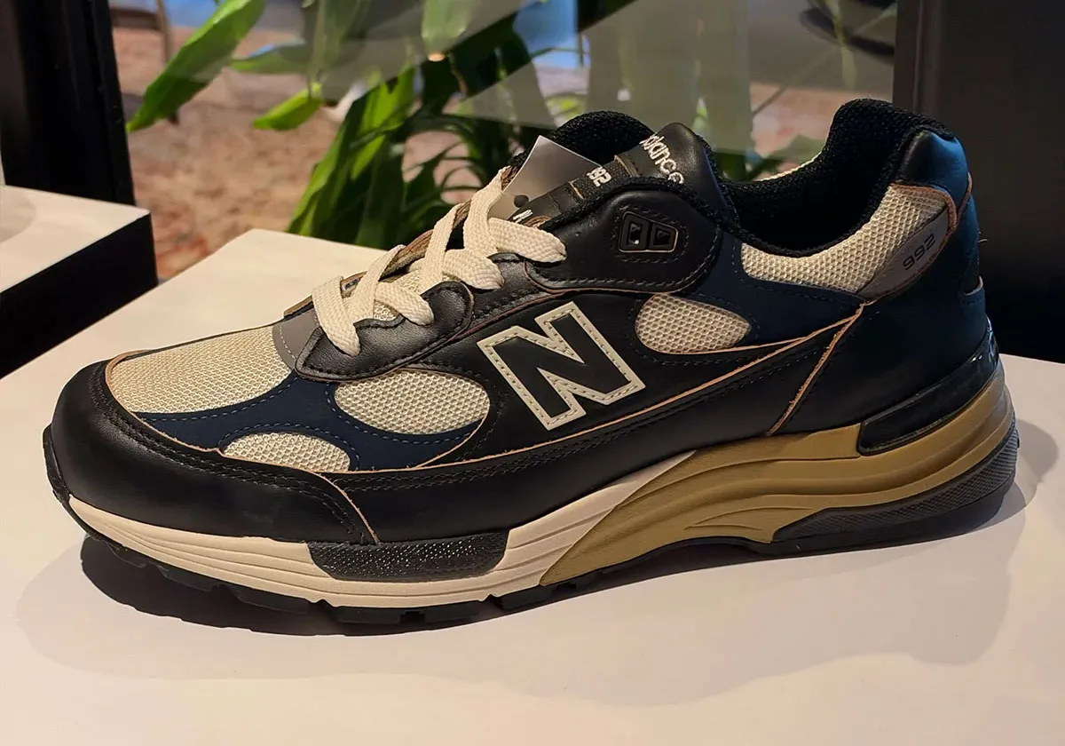Lateral view on a white display table, black leather with cream mesh and tan midsole, plant, New Balance 992 “Afterglow”
