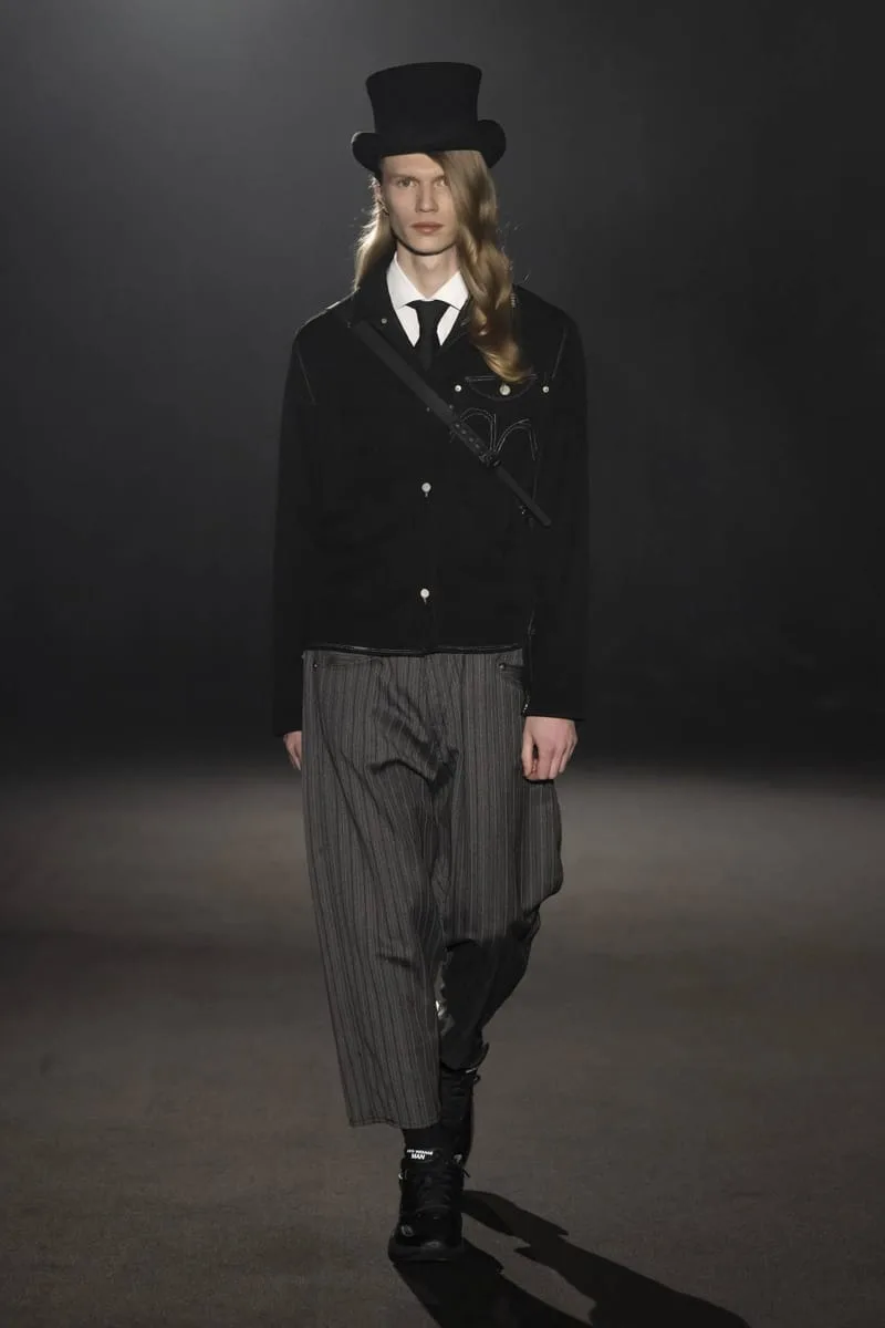 Runway model in a top hat, black jacket and wide pinstripe trousers, wearing black sneakers, Watanabe MAN P400
