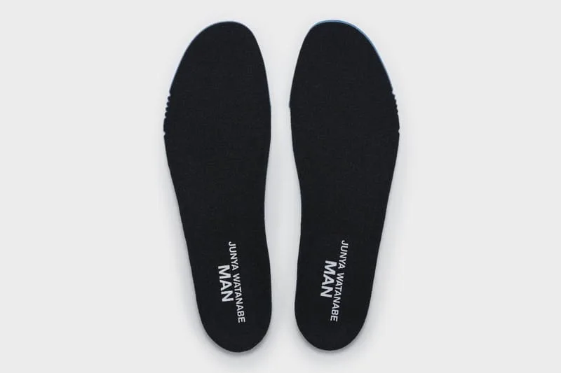 Top-down view of a pair of black insoles printed with white Junya Watanabe MAN text, blue edge showing, Watanabe MAN P400