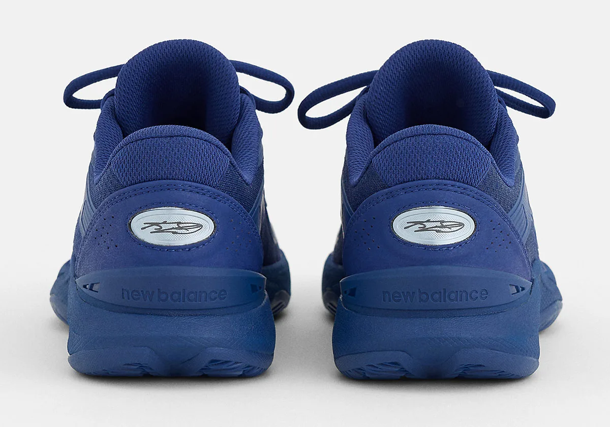 Heel view of blue pair with silver oval signature badge and new balance text on heel clip, Balance Kawhi 5