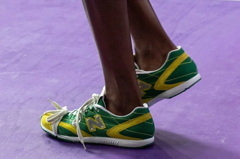On-foot lateral view of green mesh sneaker with yellow side stripe and grey N logo on purple floor, New Balance RC150