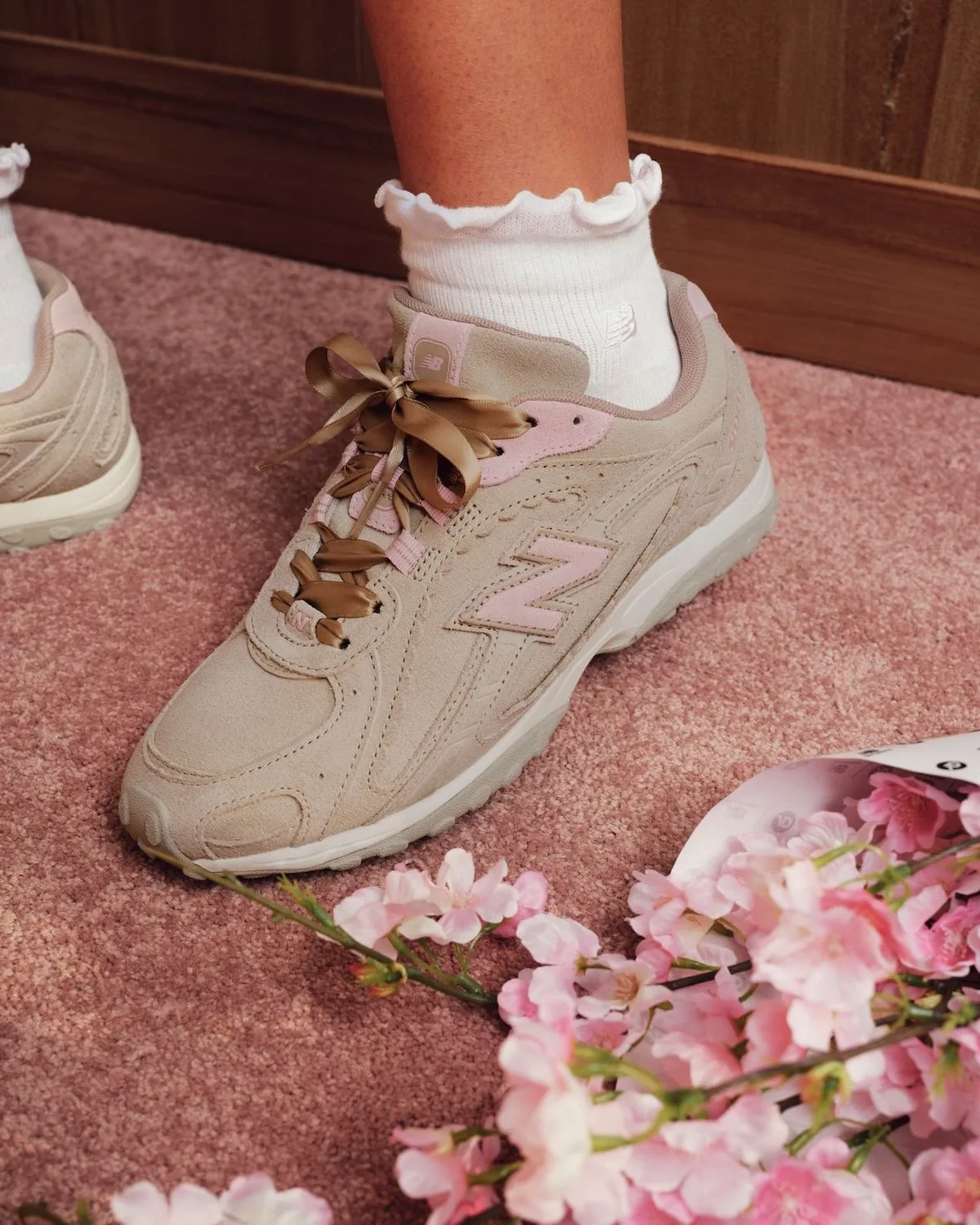 On-foot lateral of tan suede sneaker with gold ribbon laces, frilly sock and pink blossoms, Sakura